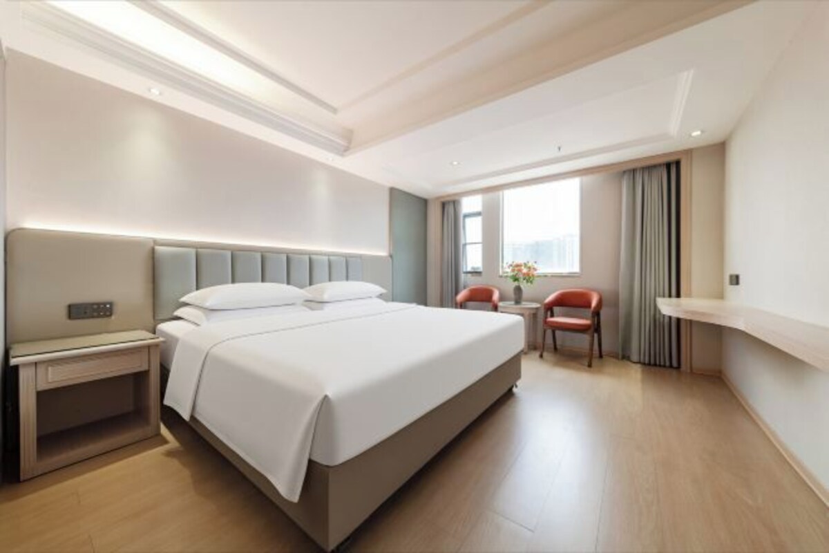 A hotel room with a large bed, bedside table, and a chair.