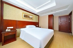 Relax in a spacious room with a large bed, wooden headboard, and a nightstand featuring a telephone and a small drawer.