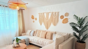 A modern living room with a beige sectional sofa, a round wooden coffee table, a potted plant, and macrame wall art.