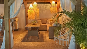 Un espacio al aire libre acogedor con mesa de madera, sillas con cojines y lámparas colgantes.