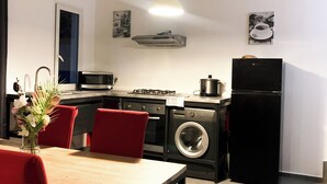 A compact kitchen with a dining area, including a table, chairs, a washing machine, a refrigerator, and a microwave. - Two-bedroom apartment Grand fond Saint-Leu vacation residence (Saint-Leu)
