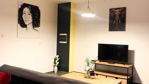A modern living room with a sofa, a TV on a wooden stand, and artwork on the walls. - Two-bedroom apartment Grand fond Saint-Leu vacation residence (Saint-Leu)