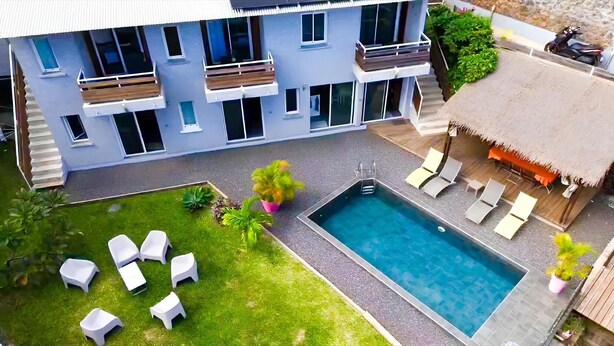 A modern hotel with a swimming pool, outdoor seating, and a thatched-roof structure. - Two-bedroom apartment Grand fond Saint-Leu vacation residence (Saint-Leu)