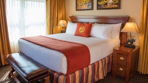Ein Hotelzimmer mit einem großen Bett, einer Bank, zwei Nachttischlampen, einem Nachttisch mit Lampe und zwei gerahmten Bildern an der Wand.