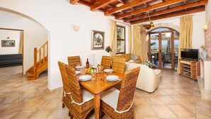 A dining area with a wooden table and wicker chairs, a sofa, and a television stand.