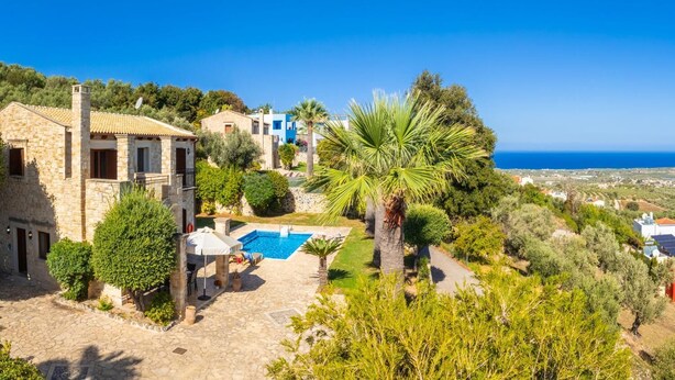 A stone villa with a swimming pool, surrounded by lush greenery and a view of the sea.