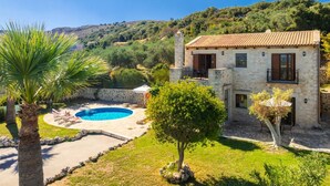 A two-story stone house with a swimming pool, surrounded by lush greenery and hills. - Villa Top Hill - Three Bedroom Villa, Sleeps 6 (Agia Triada)