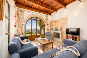 Una sala de estar con chimenea, televisor y vistas al campo a través de amplios ventanales.