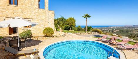 A stone villa with a swimming pool, outdoor furniture, and a view of the sea.
