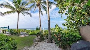 A patio area with a view of the ocean, palm trees, and a barbecue grill. - Beachfront Bliss on Longboat Key- Steps to the sand (Longboat Key)