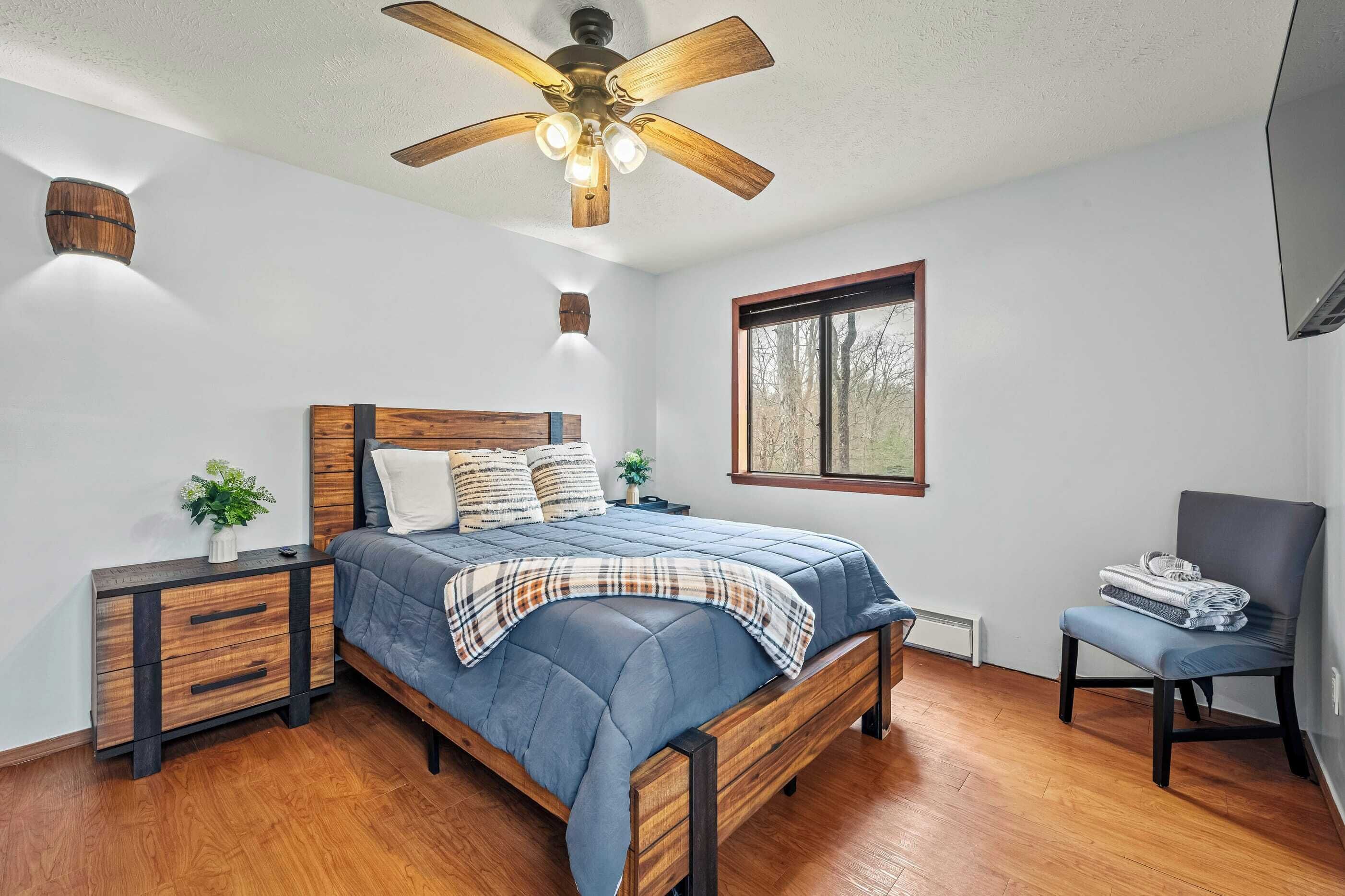 A bedroom with a wooden bed, a nightstand, a chair, a ceiling fan, and a window.
