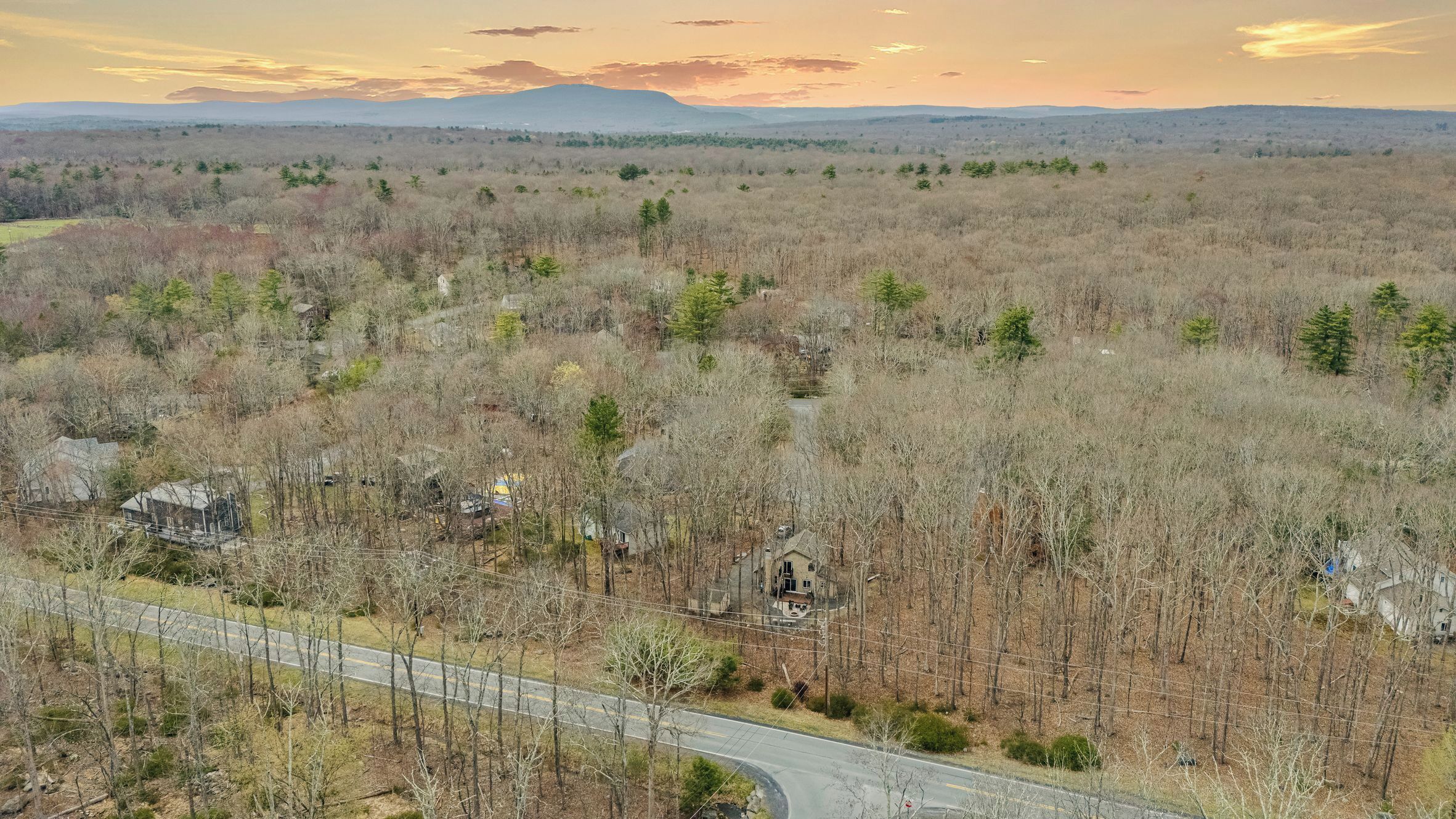 A rural landscape with a winding road, scattered houses, and a mountain range in the distance.