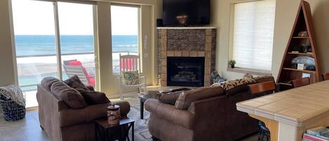 A spacious living room with a fireplace, large windows overlooking the ocean, and a cozy seating area.
