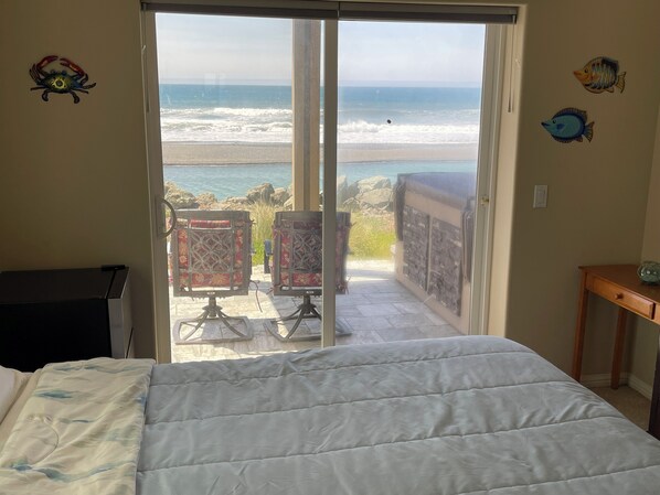 A bedroom with a bed, a desk, and a view of the ocean through a sliding door.