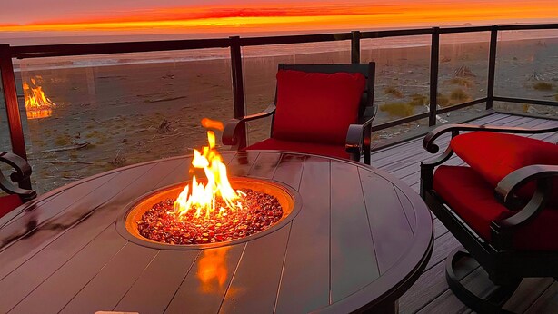 Une terrasse avec un foyer, des chaises rouges et une vue sur le coucher de soleil sur l’océan.