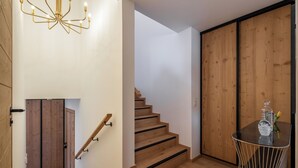 A modern interior with a wooden staircase, a chandelier, and a small table with a vase. - Écrin – Stylish alpine escape in Alpe d'Huez (Alpe d`Huez)