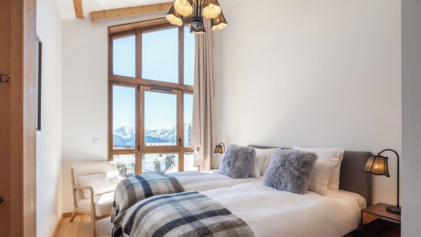 A bedroom with a large bed, a chair, a desk, and a window with a mountain view. - Écrin – Stylish alpine escape in Alpe d'Huez (Alpe d`Huez)