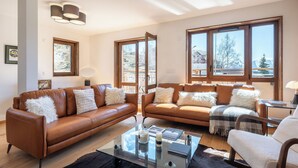 A modern living room with two brown leather sofas, a glass coffee table, and large windows offering a view of a snowy landscape. - Écrin – Stylish alpine escape in Alpe d'Huez (Alpe d`Huez)