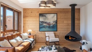 A cozy living room with a leather sofa, a white armchair, a fireplace, and a large abstract painting on the wall. - Écrin – Stylish alpine escape in Alpe d'Huez (Alpe d`Huez)