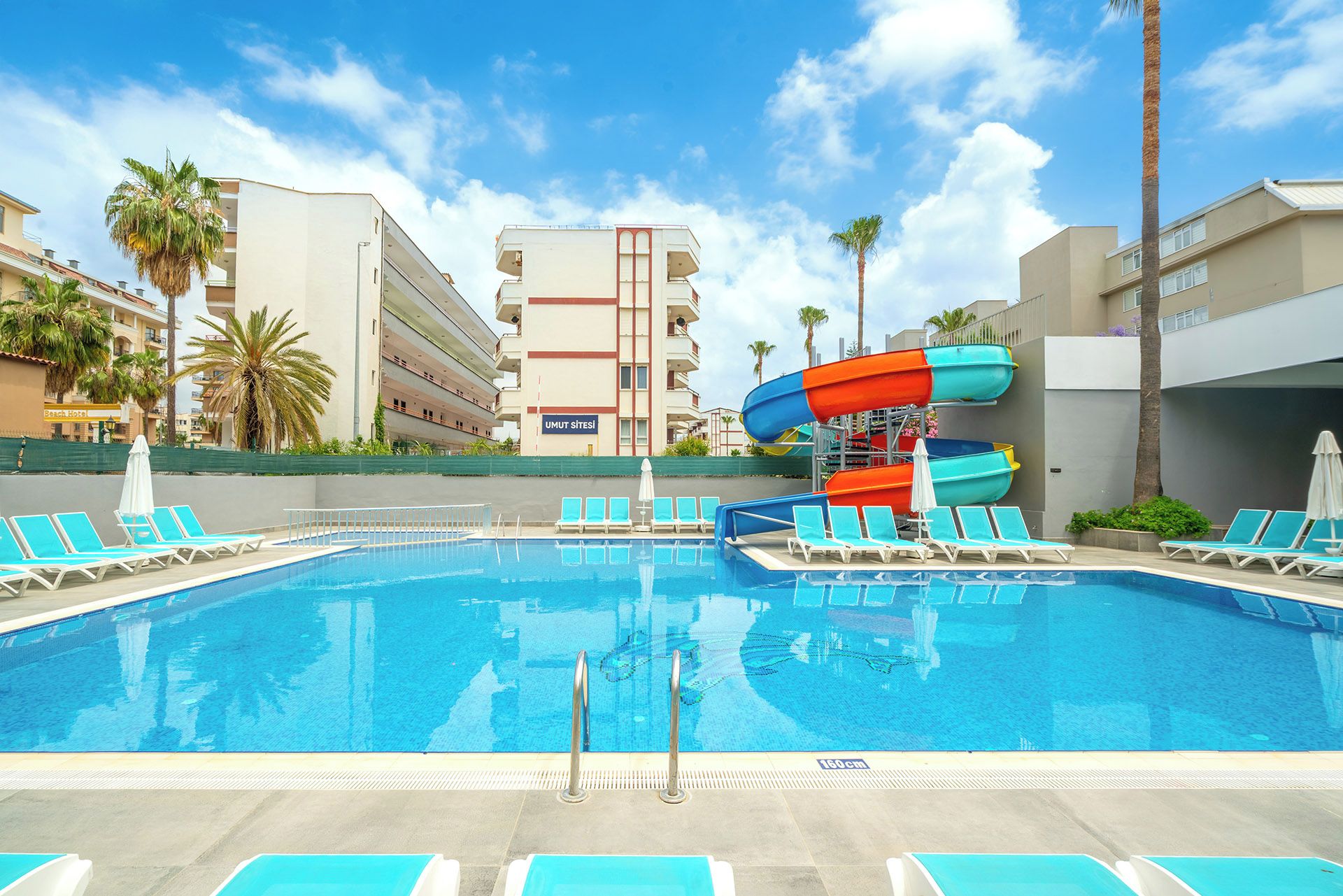 A swimming pool with water slides, lounge chairs, and a hotel building in the background.