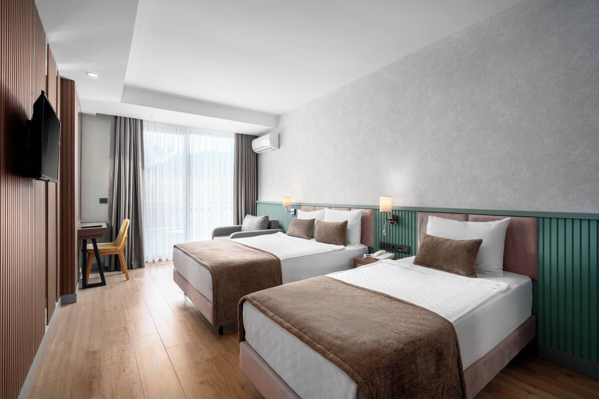 A hotel room with two beds, a desk, a chair, and a TV.