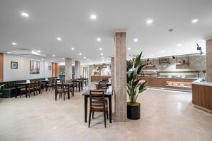A spacious dining area with multiple tables and chairs, a central column, and a large potted plant. - Sun Heaven Queen (Alanya)