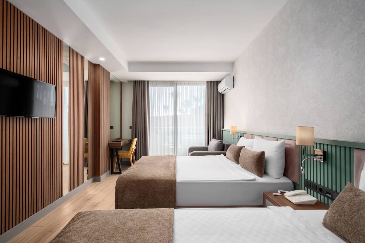 A hotel room with two beds, a TV, a desk, and a view of the outdoors.