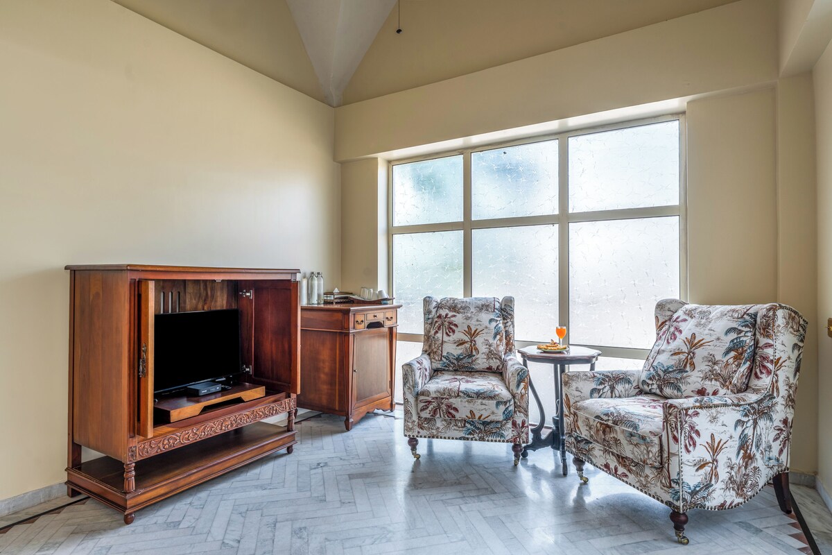 Een kamer met een houten entertainmentmeubel, twee gestreepte fauteuils, een bijzettafeltje en een groot raam.