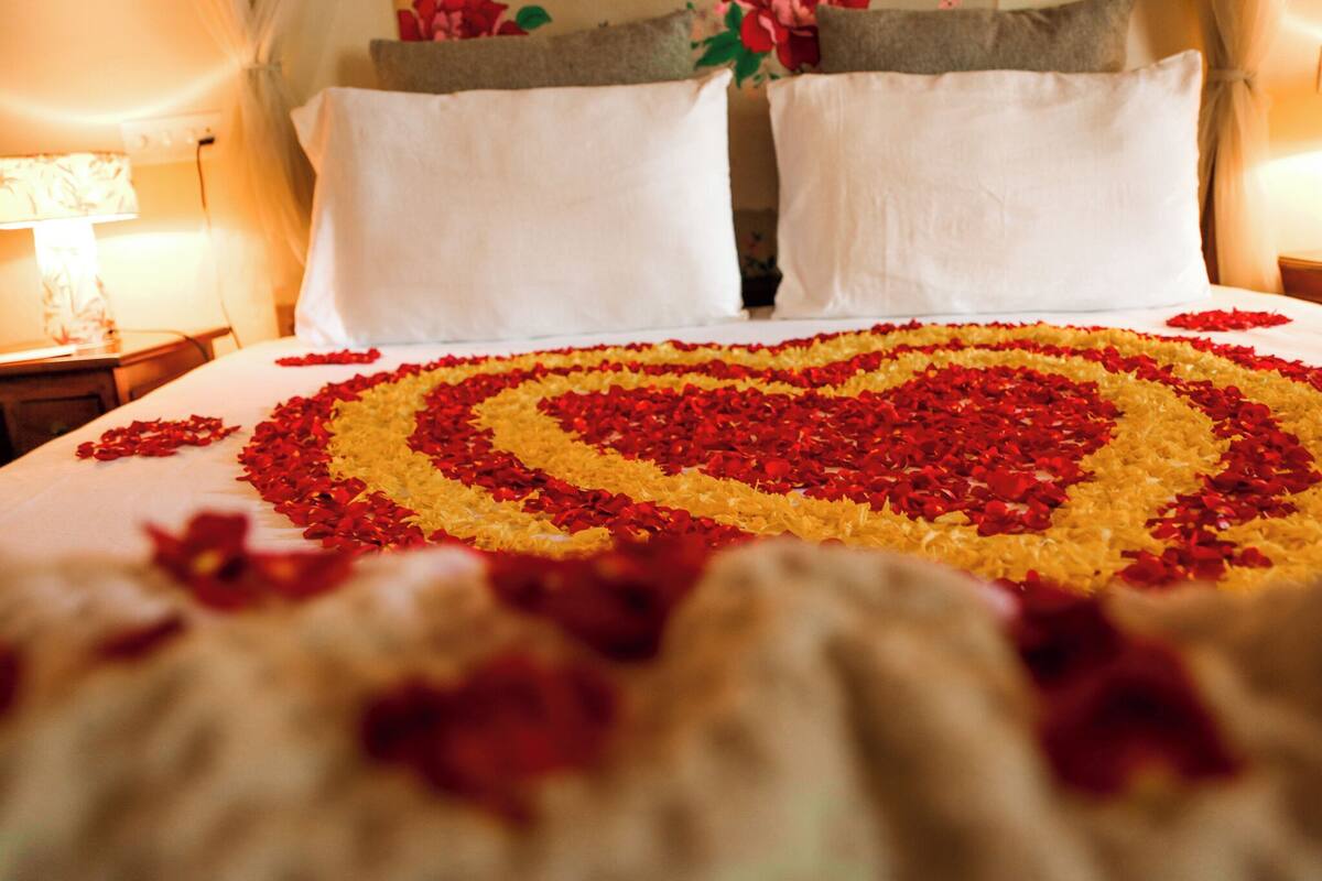 Een bed met een bloemstuk in de vorm van een hart, bestaande uit rode en gele bloemen.