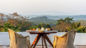 A dining table with chairs on a terrace overlooking a mountainous landscape.