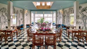 A dining area with checkered flooring, wooden tables, and chairs, surrounded by walls with black and white plant illustrations.