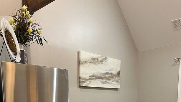 Un espacio habitable compacto con un refrigerador de acero inoxidable, un sofá de cuero oscuro, una mesa de centro con dos tazas negras y un cuadro en la pared.