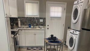 Cocina compacta con gabinetes blancos, horno integrado, microondas, lavaplatos y lavadora.