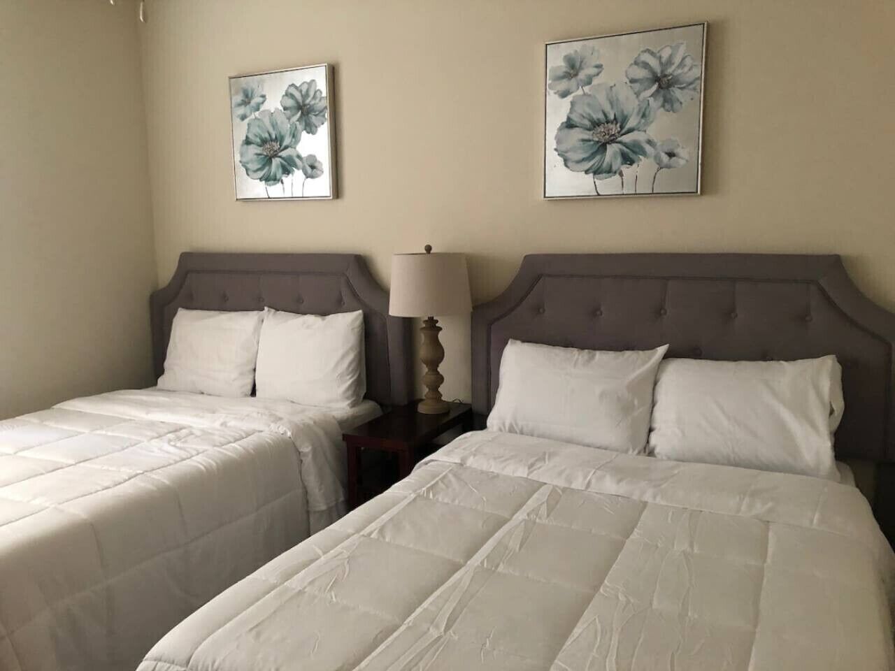 A hotel room with two beds, each with white bedding and a headboard. There are two framed floral paintings on the wall above the beds.