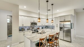 A modern kitchen with white cabinets, a marble island, stainless steel appliances, and hanging pendant lights.