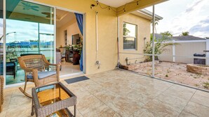 A spacious patio with a glass door leading to an indoor area, wicker furniture, and a view of the surrounding landscape.