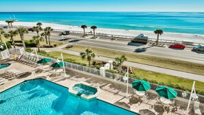 Zona de piscina con vista a la playa y al océano, una calle con coches aparcados y un paseo vallado con sombrillas.