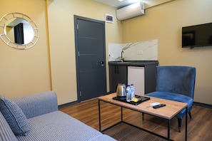 A compact hotel room with a sofa, a small table with a kettle, water bottles, and a remote control. - La Vitinre (Istanbul)