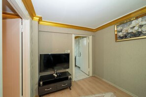 A room with a flat-screen TV on a black stand, a wooden floor, and a framed floral painting on the wall. - La Vitinre (Istanbul)