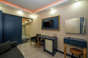A modern hotel room with a sofa, a desk with a chair, a TV mounted on the wall, and a small cabinet. - La Vitinre (Istanbul)