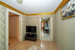 A living room with a TV on a stand, wooden flooring, and a dining area visible through an open door. - La Vitinre (Istanbul)