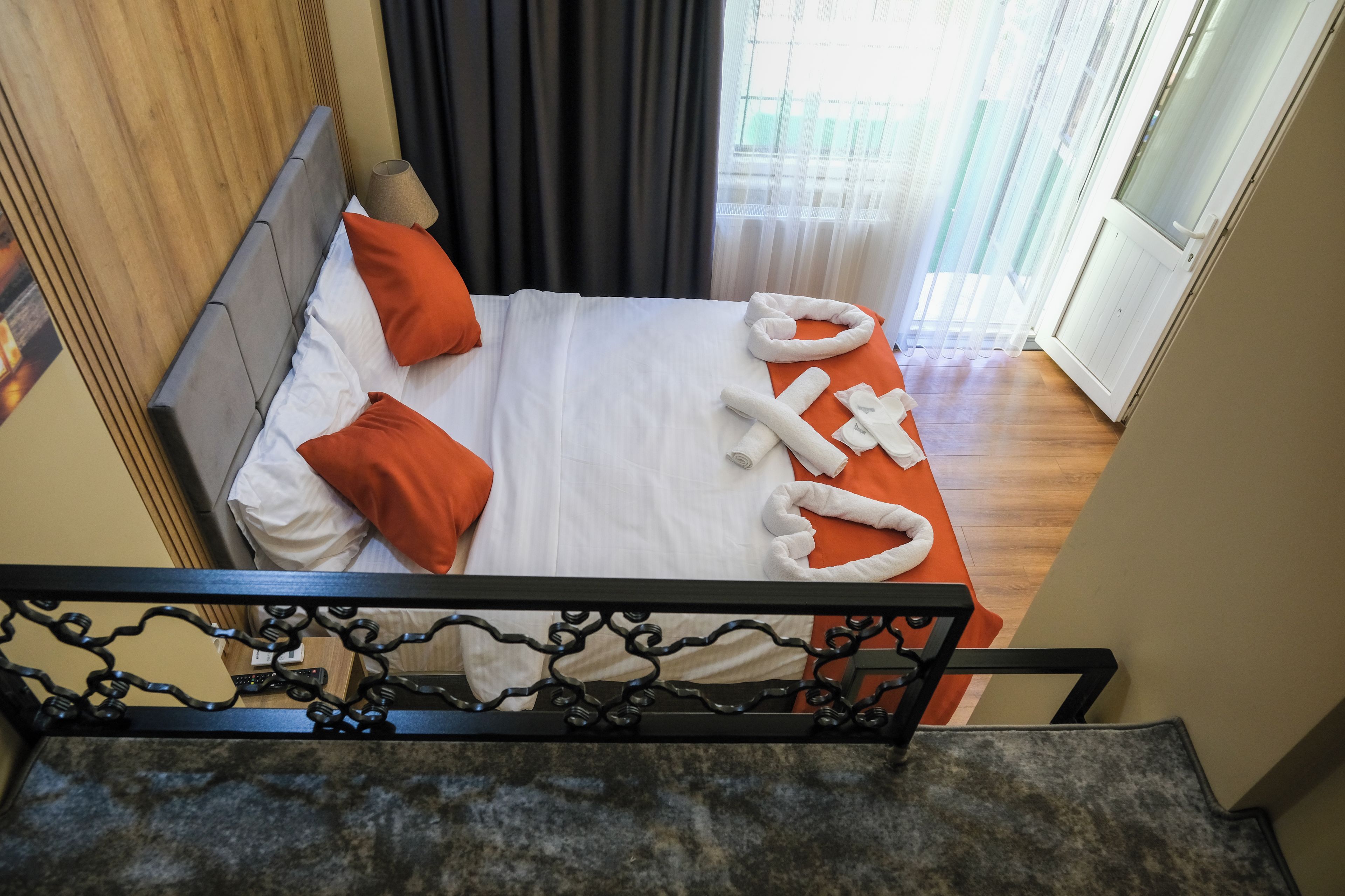 A hotel room with a bed, orange pillows, white linens, and a towel arrangement.