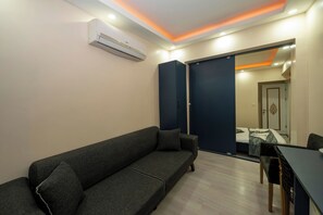A modern room with a dark grey sofa, a small table, and a bed with a blue and white bedspread. - La Vitinre (Istanbul)
