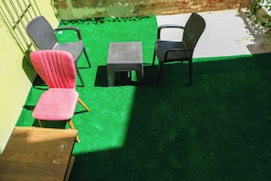 A patio area with green artificial turf, two black chairs, a small wooden table, and a pink chair. - La Vitinre (Istanbul)