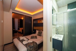 A hotel room with a bed, bedside table, mirror, and a bathroom with a sink and shower. - La Vitinre (Istanbul)