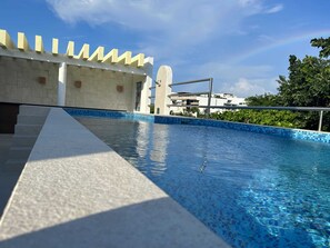 A swimming pool with a tiled edge, a stone staircase, and a white building with a unique architectural design in the background. - Tropical Elegance Studio CondoHotel  (Puerto Morelos)
