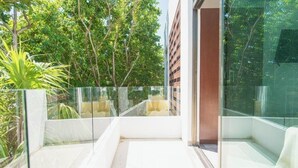 A modern balcony with glass railings, a white floor, and lush greenery in the background. - Tropical Elegance Studio CondoHotel  (Puerto Morelos)