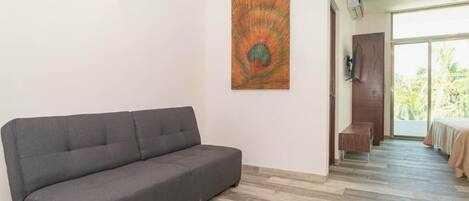 Un salon moderne avec un canapé gris, un grand tableau abstrait accroché au mur et une vue sur la verdure grâce à une porte coulissante.