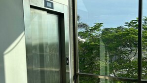 A modern elevator with a metallic finish, adjacent to a large glass door with a view of greenery and trees outside. - Tropical Elegance Studio CondoHotel  (Puerto Morelos)
