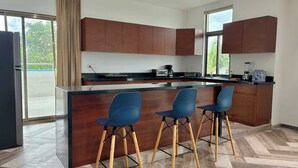 A modern kitchen with a central island, wooden cabinets, and three blue bar stools. - Tropical Elegance Studio CondoHotel  (Puerto Morelos)